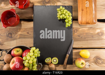 Slate server/board/tray with space for text on rustic wood planks. Arranged fruits: kiwi, apples, lemon, grapes. Menu board for restaurant. Stock Photo