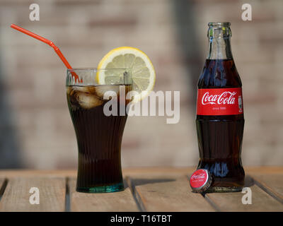 HOEILAART, BELGIUM - MAY 17 2017: A coca cola bottle next to a coke glass, filled with ice cubes and a slice of lemon. Stock Photo