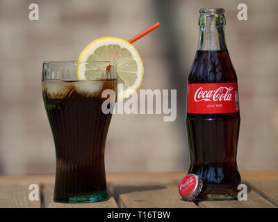 HOEILAART, BELGIUM - MAY 17 2017: A coca cola bottle next to a coke glass, filled with ice cubes and a slice of lemon. Stock Photo