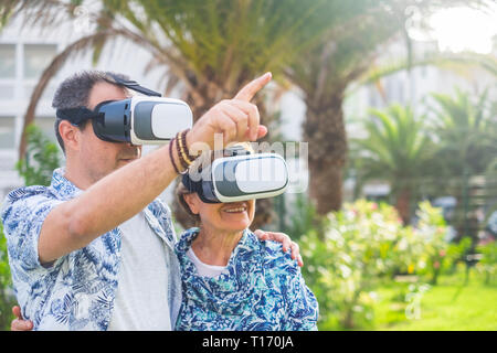 Adult couple mixed generations diversity have fun together in outdoor using goggles headset for virtual reality - people and technoogy concept Stock Photo