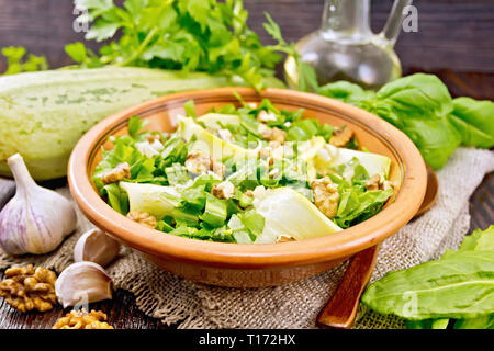 Salad of young zucchini, sorrel, garlic and nuts, seasoned with vegetable oil in a plate on napkin of sackcloth on a wooden board background Stock Photo