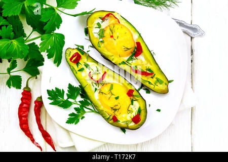 Scrambled eggs with hot peppers in two halves of avocado in a plate, fork, parsley on a wooden background from above Stock Photo