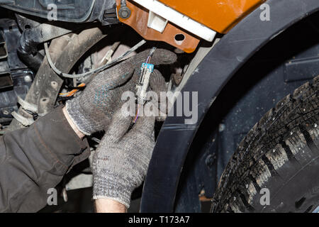 Close-up on the hands of the master in protective gloves connecting the connector with the wires in the electrical circuit of the car under the bumper Stock Photo