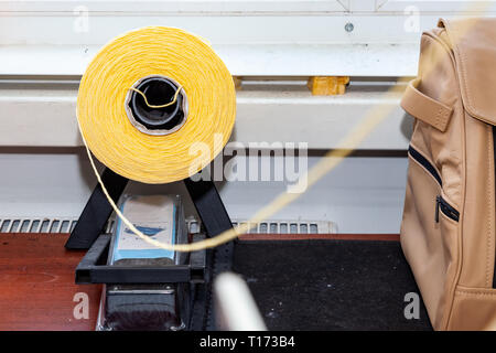 One big yellow bobbin with large mating colored threads in the studio for interior design workshop on the table with thread stretching towards the cam Stock Photo