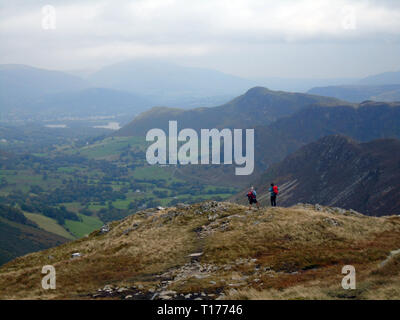 Two Hikers Looking down the Newlands Valley Towards Cat Bells from the Wainwright Robinson in the Lake District National Park, Cumbria, UK. Stock Photo