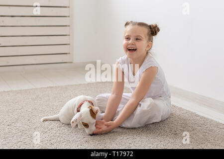 People, pets and animal concept - Little girl sitting on the floor over white background and holding puppy Jack Russell Terrier Stock Photo