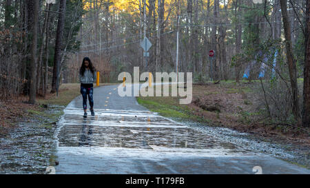 Woman walking on pathway after rain storm with puddles and reflections in the foreground Stock Photo