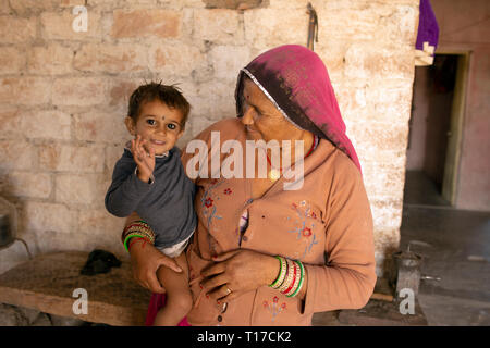 A Bishnoi girl smiles and waves while being held by her grandmother. Stock Photo