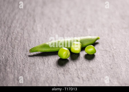 One whole green sugar snap pea pod and three peas on grey stone Stock Photo