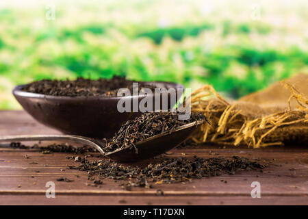 Lot of pieces of dry black tea earl grey in a grey ceramic bowl on jute cloth with silver spoon green tea field behind Stock Photo