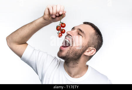 This is how vegan like raw and good farmer vegetables. Man is holding a ramus of ripe and red small tomatoes and want to swallow them. He is ready to Stock Photo