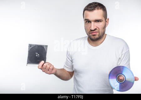 Young man holding a compact disk in one hand and a box from it in another hand and staring at camera. Time goes so fast that now he doesn't know what Stock Photo