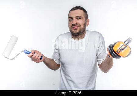 Young man standing in a room and holding brush for painting and headphones. He wonders how to do repairs himself. Isolated on white background. Stock Photo