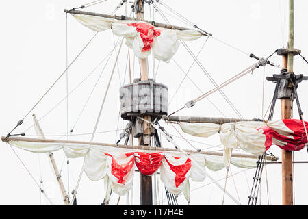 Tackles of an old sailing vessel - a mast, a mast, raised red-white sails, ropes. Stock Photo