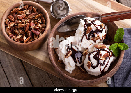Overhead view of vanilla ice cream topped with chocolate syrup and pecans in a wooden bowl Stock Photo