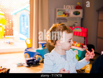 young girl looking down at messy hand,fingers appear to have ketchup on them as she is about to lick them clean. Stock Photo