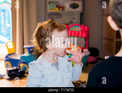 young girl mouth wide open about to lick messy fingers,which appear to have ketchup on them,partial view of brother in the foreground watching her. Stock Photo