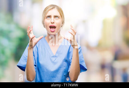 Young beautiful blonde doctor surgeon nurse woman over isolated background crazy and mad shouting and yelling with aggressive expression and arms rais Stock Photo