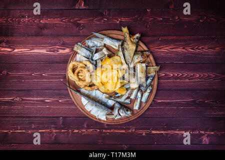 Snacks for beer. Salted, dried fish, squid rings and potato chips, on the cutting board and wooden background Stock Photo