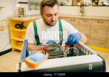 Worker in uniform testing refrigerator at home Stock Photo
