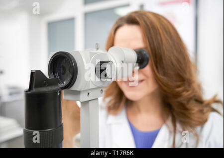 Close up of ophthalmologist looking in slit lamp. Beautiful woman working in medical clinic and examining eyesight using special equipment, eye test machine. Concept of health care. Stock Photo