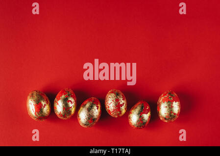 Six golden colored and decorated with sparkles Easter eggs on red background. Stock Photo