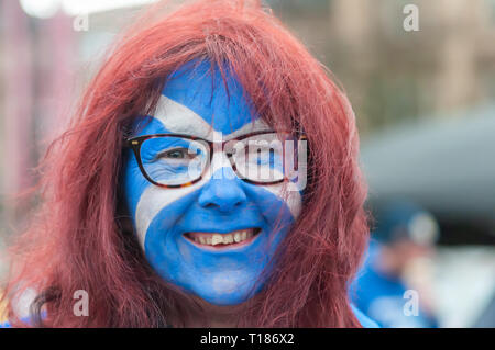Glasgow, Scotland, UK. 24th March, 2019. A smiling woman with red hair, wearing glasses and the flag of Scotland painted on her face joins campaigners in support of Scottish Independence as they gather for a rally in George Square.The rally was organised by the group Hope Over Fear. Credit: Skully/Alamy Live News Stock Photo