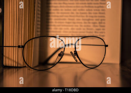 Close up of glasses laying on a table in front of a open book Stock Photo