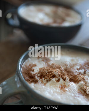two big mugs of a hot foamy drink covered in whip cream and cinnamon Stock Photo