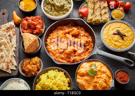 Various Indian dishes on a table. Spicy chicken Tikka Masala in iron pan. Served with rice, naan and spices. Set of different kind Indian food. Stock Photo