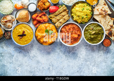 Composition of Indian cuisine in ceramic bowls on stone table. Tikka masala, butter chicken, Nilgiri, seekh kebab, rice, Onion Bhajia, paneer, samosa, Stock Photo
