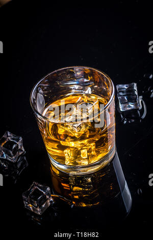 Whisky, whiskey or bourbon in glass with ice cubes on black reflection background