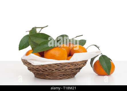 Juicy tangerines, small oranges with leaves in wicker basket with serviette, napkin. Fresh fruit on white, isolated against background. Stock Photo