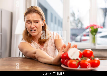 Dark-eyed mature woman not eating tomatoes while feeling allergic Stock Photo
