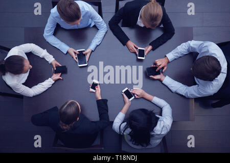 Business people with smartphones sitting around the table, top view Stock Photo
