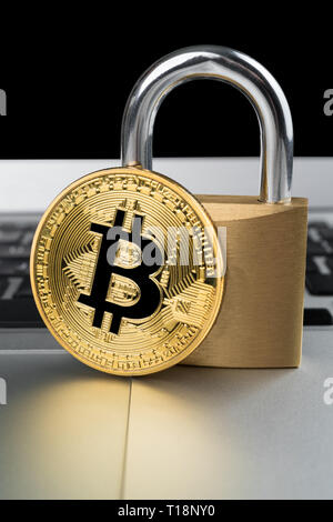 Physical bitcoin with padlock on a laptop computer keyboard. Cyber cryptocurrency security abstact concept. Vertical orientation. Stock Photo