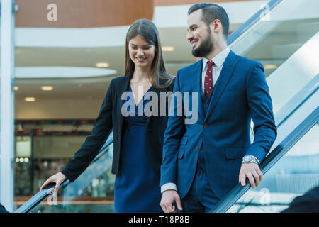 Business couple on escalator talking and smiling Stock Photo