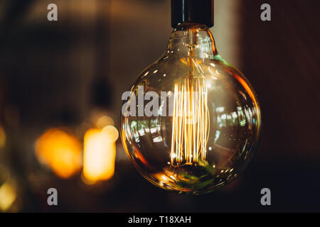 close-up of a round huge light bulb glows in golden color against a dark background in the interior Stock Photo