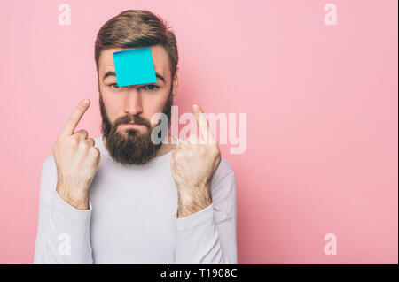 Strange guy has put a blue sticker on his forehead. He is pointing at it with fingers on both hands. Isolated on pink background Stock Photo