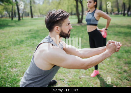 Young people are warming up. He is doing squats while she is stratching her legs behind him. They are wokring separately from each other Stock Photo
