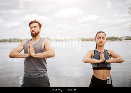 Calm and peaceful picture of young man and woman meditating. They are keeping their hands together and standing with their eyes closed. They are stand Stock Photo