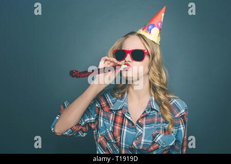 Funny girl is celebrating her birthday. She is holding whistle in her mouth and holding it with a hand. Also she has her sunglasses on and a birthday  Stock Photo