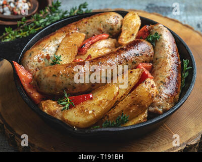 grilled chicken sausages with fried potatoes and peppers in an iron pan Stock Photo