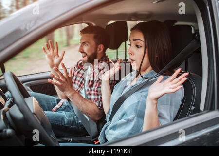 Two young people are riding in car. Girl is not keeping hands on rudder. She is amazed. Guy is screaming and keeping his hands in air. There is going  Stock Photo