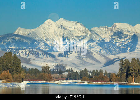 moon rising over the flathead river and mission mountains in winter near dixon, montana Stock Photo