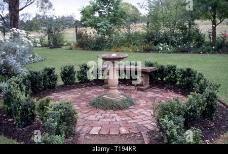 CIRCULAR BRICK GARDEN EDGED WITH SMALL HEDGES, CENTRE BIRD BATH WITH MONDO GRASS GROWING AROUND BASE. NEW SOUTH WALES, AUSTRALIA Stock Photo