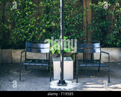 Two black chairs in smoking area on green tree background. Stock Photo