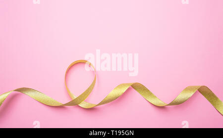 Golden shiny ribbon on pink color background, copy space, top view. Decoration, gifts concept Stock Photo