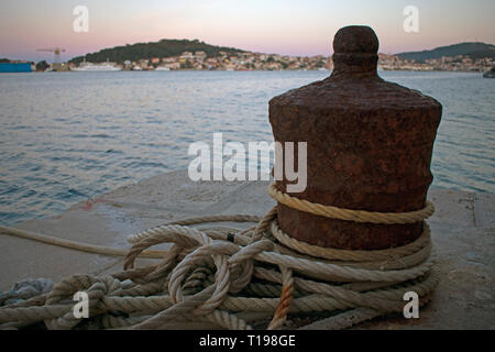 Close up of rusty boat mooring with ropes wrapped around and town in background Stock Photo