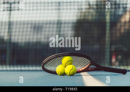 Three tennis balls on a professional racket on acrylic blue surface Stock Photo